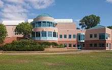 A beige building with a large windowed rotunda stands before a wide lawn.