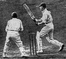 A cricketer has just hit a ball away, watched by the wicket-keeper