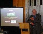 Minister Pete Hodgson leaning on a lectern, with an image displayed on a screen