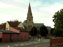 A church seen beyond houses and tress with a prominent tower and spire