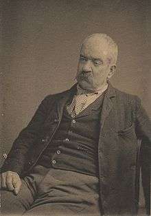 portrait photograph of seated artist with mustache and gray hair