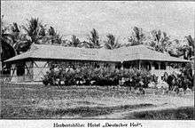 small single story building, grass roof, veranda, bushes