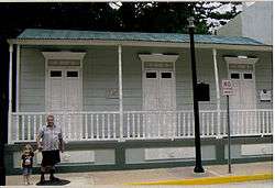 Photograph of the Barbosa House, a modest, one-story house with a corrugated roof and a veranda facing the street