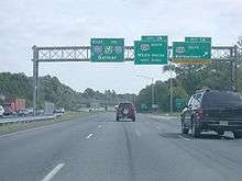 A six-lane highway at an interchange with three green signs over the road. The left sign reads east Interstate 195 to New Jersey Turnpike Interstate 95 Belmar, the middle sign reads exit 1B U.S. Route 206 north White Horse next right, and the right sign reads exit 1A U.S. Route 206 south Bordentown upper right arrow exit only.