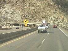 A sharp curve with a cut in the mountain visible to support the highway