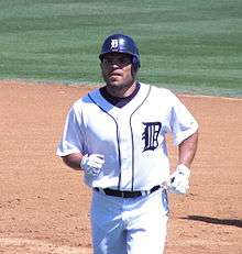 Man in a white baseball uniform and navy-blue helmet jogs on a baseball field