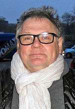 A photo of Janusz Kamiński wearing a white scarf and a black bubble vest.