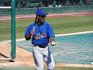 A man, holding a baseball bat and ball in hand, prepares to hit the ball.