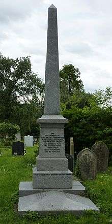 A polished, grey, obelisk-like funerary monument surmounting a grave