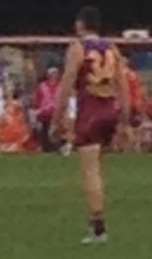 A man wearing a maroon, blue and gold jumper and wearing number 34 stands on grass.