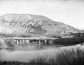 A photo of a river in the foreground and hills in the background.  A small dam or diversion is in the center of the photo where a canal flows off from the river.