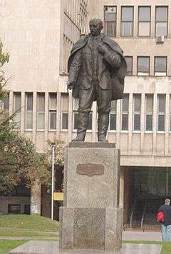 Statue of man in cape on a pedestal in front of a building