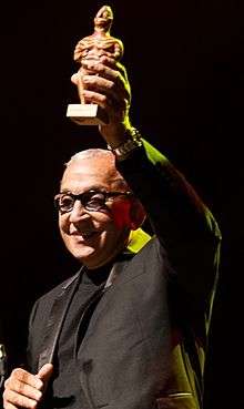 A man in a black shirt is holding an award on his left