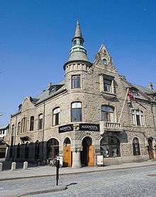 Ornate stone three-storied building encompassing a street corner, with a windowed turret and topped by a spiral.