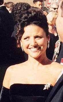 A woman with black hair tied in a knot wearing a black dress, at a crowded event.