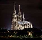 A large, brightly lit cathedral sits in the middle of a skyline at night.