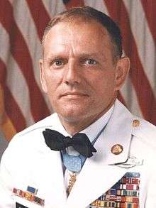 Head of a man in military dress uniform, wearing a bow tie over a white jacket.  Medal of Honor around his neck and other medal ribb0ns on his chest