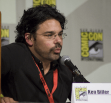 A man in a black shirt speaks into a microphone.