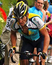 Close-up image of Armstrong with a strained look on his face as he climbs a mountain. Spectators are visible behind him.