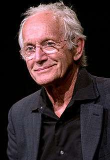 A white-haired man in a tuxedo looks off to one side, smiling