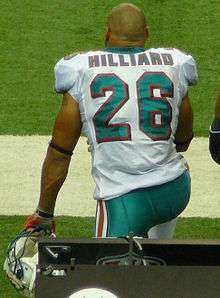 Man in football uniform kneeling on the sidelines with helmet off