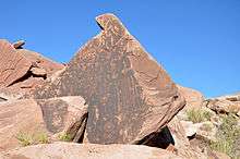 Images of animals, people, and geometric figures incised on the dark vertical face of a large rock