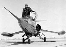 Pilot in overall black suit crouching on jet aircraft's nose