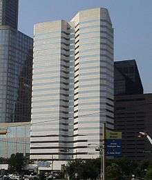  Two attached concrete and glass office towers, one with an irregular shape. Both have uniform horizontal bands of windows alternating with the concrete.