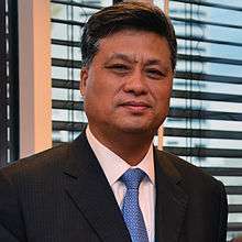 a serious looking man, wearing suit and a blue tie