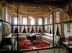 Room with many stained-glass windows, small table in center and seating along the walls