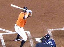 A man wearing an orange baseball uniform holding a baseball bat over his right shoulder