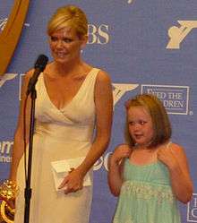 A women with blond hair, wearing white dress also holding a golden statuette.