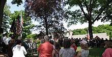 Uniformed men and civilians standing before a memorial at a park