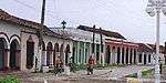 A street with single-storied colonned buildings that are painted in various colors.