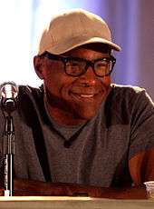 A man in a baseball cap, glasses and a grey T-shirt.