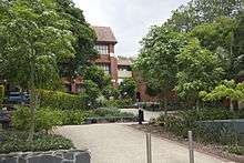 A path leading up between three red brick buildings surrounded by trees.