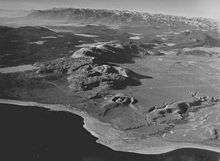 Chain of tall hills with sharp peaks. A crater and lake are in the foreground.