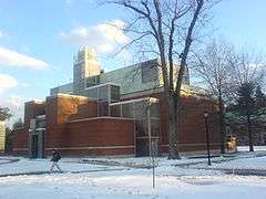 A glass and brick building rests behind a leafless tree on a snowy day