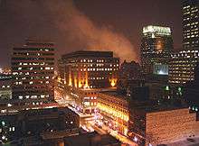 A landscape image of a city setting at night including several skyscrapers and a roadway illuminated by streetlights.