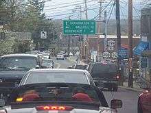 A narrow four-lane highway is jammed with cars as they wait at a signalized intersection.