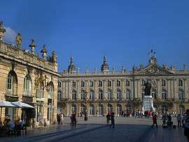 Ornate stone buildings with one two-story building from the left, foreground to the left midground. A two-story building covers the background.