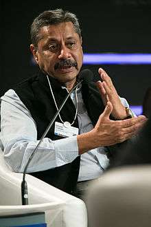 A man speaking in a conference with hand gestures.