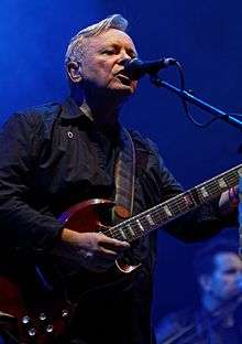 Sumner playing a guitar and singing into a microphone onstage