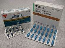 The cardboard packaging of two medications used to treat obesity.  Orlistat is shown above under the brand name Xenical in a white package with Roche branding. Sibutramine is below under the brand name Meridia. Orlistat is also available as Alli in the United Kingdom. The A of the Abbott Laboratories logo is on the bottom half of the package.