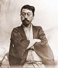 Portrait of an Asian man with moustache dressed in traditional Japanese clothes. He is looking down with his arms crossed.