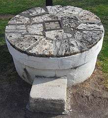 A round millstone sits upon a grassy lawn.