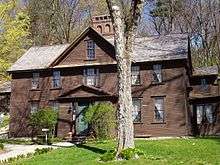 A dark brown colonial frame house with wooden shingles.