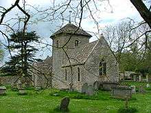 A small stone church seen from the southeast, with a central tower capped by a pyramidal roof. The chancel extends forwards and beyond the tower is the gabled south porch