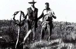 Blurry image of two men standing by tree stump with wreath