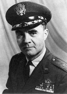 Head and shoulders of man in uniform with peaked cap. He has four rows of ribbons, pilot's wings, and  a star on each shoulder.